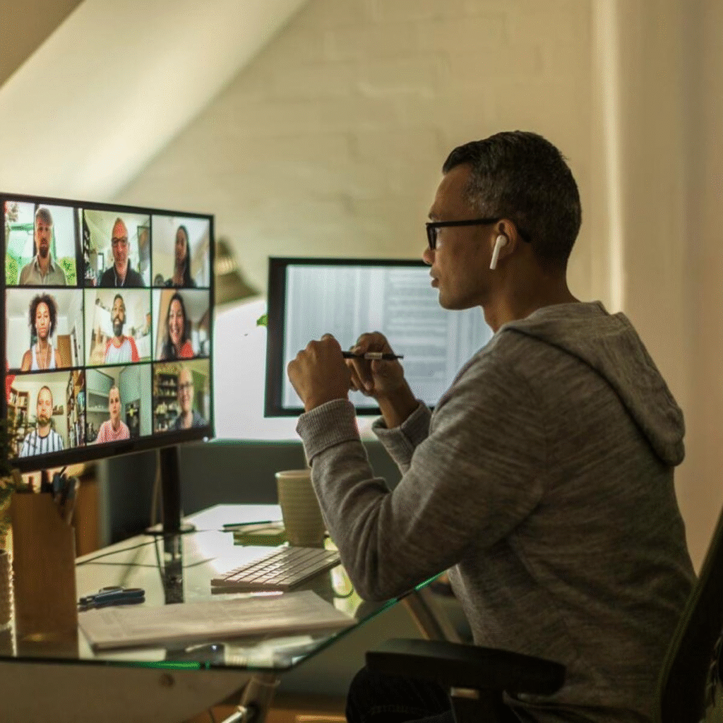 A professional working from home while participating in a virtual meeting with multiple team members on a large computer screen.